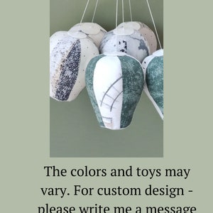 May include: A mobile made of five fabric hot air balloons in shades of green, white, and gray. The balloons are suspended from a white ceiling.