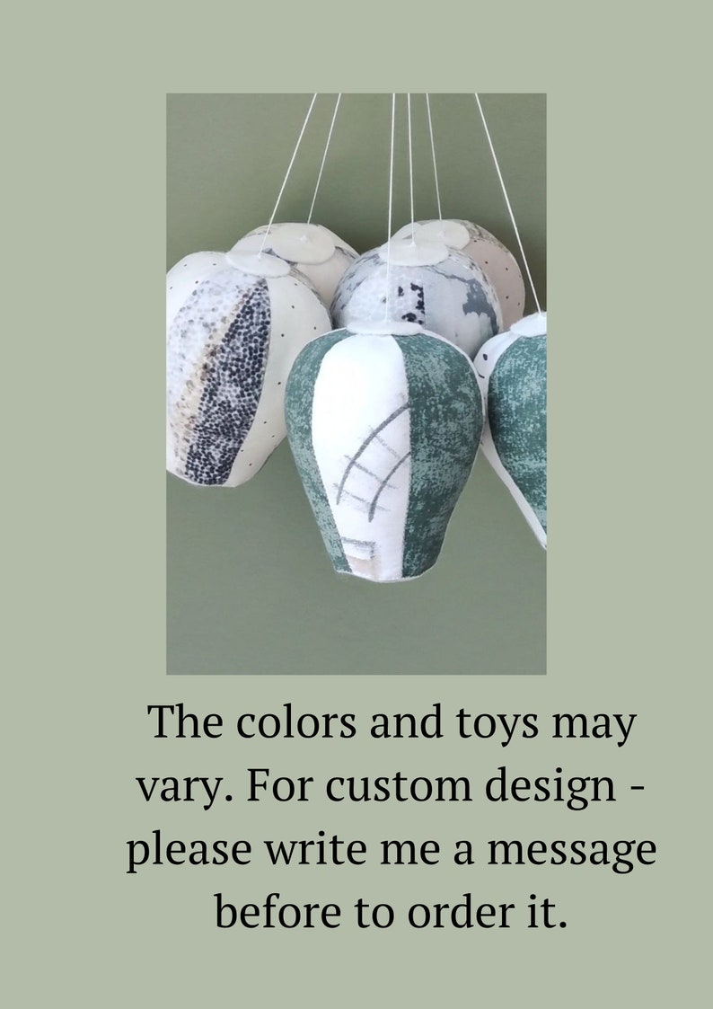 May include: A mobile made of five fabric hot air balloons in shades of green, white, and gray. The balloons are suspended from a white ceiling.