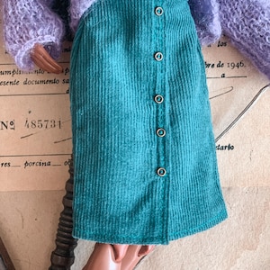 May include: A teal corduroy skirt with a button-down front. The skirt is paired with a light purple, fuzzy sweater. The background includes vintage paper with text and the number 485731.