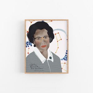 May include: A framed art print featuring a portrait of Katherine Johnson. She is depicted with dark hair, glasses, and a gray collared shirt. The background includes a constellation design and the quote "Do the Research... Ask Questions."