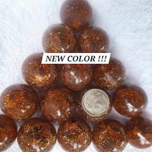 May include: A collection of amber-colored spheres, arranged in a pyramid shape, with a coin for size comparison. The spheres have a textured, speckled appearance. The text "NEW COLOR !!!" is displayed across the top.