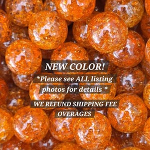 May include: Close-up of numerous orange glass marbles. The marbles have a textured, reflective surface. Text on the image reads "NEW COLOR!" and "Please see ALL listing photos for details *"