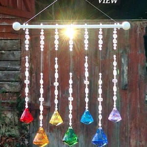 May include: A Chakra Sun Catcher with a white rod and hanging crystal prisms in red, orange, yellow, green, blue, and purple. The prisms are suspended by strings of clear beads. The text "OVERALL VIEW" and "CHAKRA SUN CATCHER" are visible.