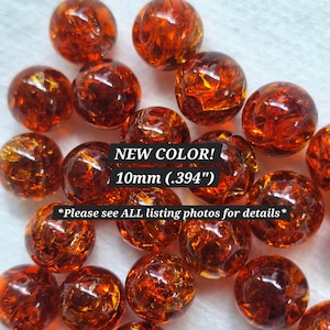 May include: A collection of round, amber-colored glass beads with a crackled texture. The beads measure 10mm (.394 inches) in diameter. Text overlay reads: NEW COLOR! 10mm (.394") *Please see ALL listing photos for details*