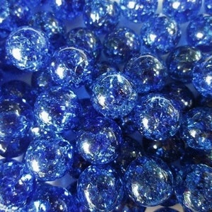 May include: A collection of round, deep blue glass beads featuring a crackled texture throughout. Each bead has a smooth, reflective surface with internal fractures that create a multifaceted appearance, catching the light across the cluster.