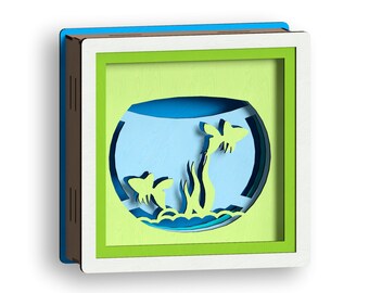 May include: A green, white, and brown wooden frame with a blue, green, and white paper cutout of a fish tank with two fish and plants inside.