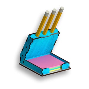 Może przedstawiać: Niebieski drewniany organizer biurkowy z wbudowanym uchwytem na notes. Organizer ma miejsce na ołówki i przegródkę na karteczki samoprzylepne. Uchwyt na notes ma różową karteczkę samoprzylepną i stos kolorowych karteczek samoprzylepnych.