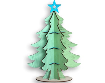 Puede incluir: Un árbol de Navidad de madera con una estrella azul en la parte superior. El árbol está pintado en tonos verdes y tiene una textura de veta de madera.