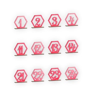 May include: Set of 24 pink wooden table number place cards. Each card is shaped like a hexagon and features a white number from 1 to 24.