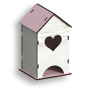 Puede incluir: Una caja de madera blanca con forma de casa con un techo rosa y un recorte en forma de corazón. La caja tiene una base rosa y una pequeña abertura en la parte inferior.
