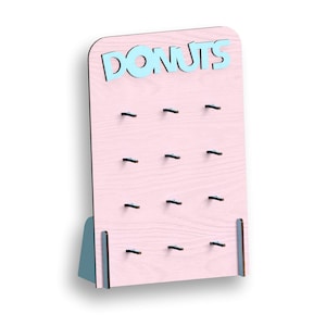 May include: A pink wooden donut wall with 12 hooks for hanging donuts. The wall has the word "DONUTS" in blue letters at the top.
