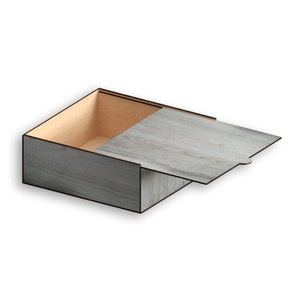 Può includere: Una scatola di legno con un coperchio incernierato. La scatola è realizzata in legno grigio chiaro con una venatura del legno. Il coperchio è aperto e l'interno della scatola è realizzato in legno marrone chiaro.