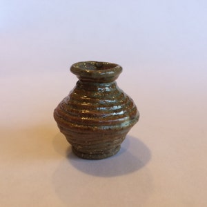 May include: A small, brown and green ceramic vase with a rounded body and a wide, slightly flared opening. The vase has a textured, ribbed surface.