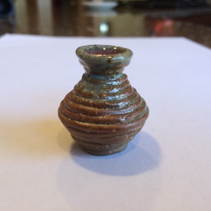 May include: A small, brown and gray ceramic vase with a coiled design. The vase has a rounded body and a flared opening.