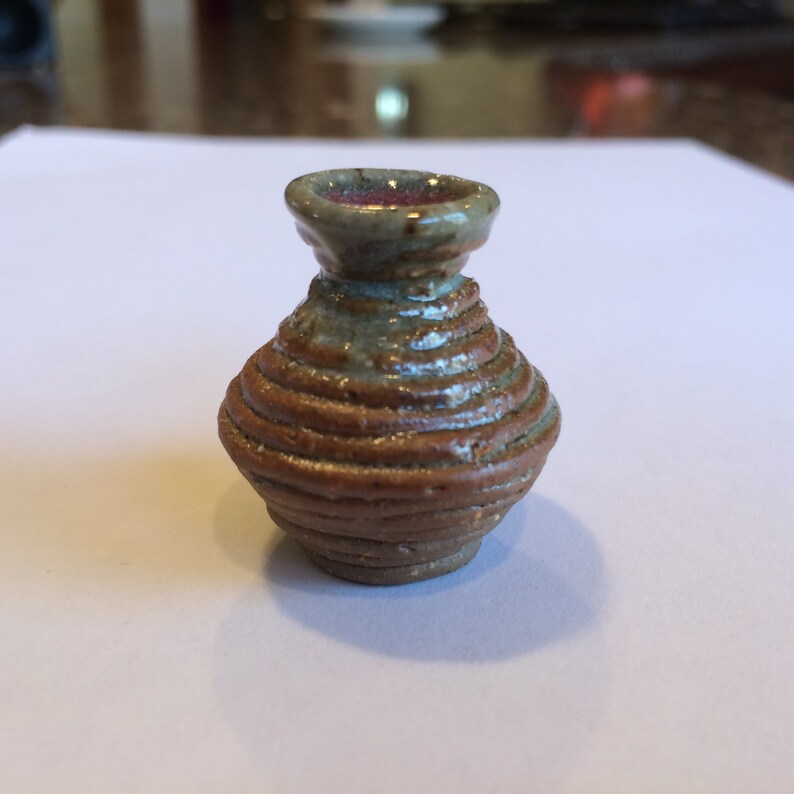 May include: A small, brown and gray ceramic vase with a coiled design. The vase has a rounded body and a flared opening.