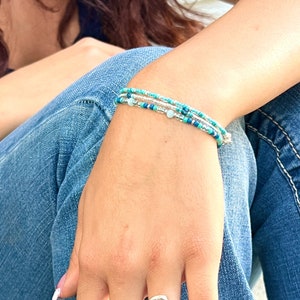 May include: A silver ring with a blue oval gemstone. The ring is worn on the index finger of a hand with white and pink nail polish.