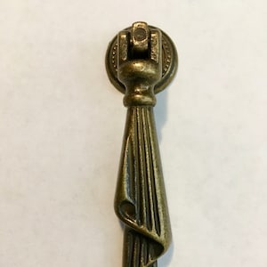 May include: A gold-toned metal cabinet pull with a decorative, twisted design. The pull has a round base with a small knob on top.