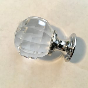 May include: A clear crystal cabinet knob with a faceted design and a silver base.