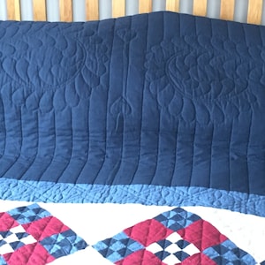 May include: A blue quilted bedspread with a floral pattern. The bedspread is folded over a white bed with a red, white, and blue quilt underneath.