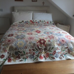 Peut inclure: Un lit blanc avec une courtepointe florale. La courtepointe présente une variété de couleurs, notamment le rose, le rouge, le bleu et le vert. La courtepointe est faite de chutes de tissu et a un design en patchwork.