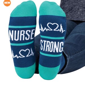 Op de afbeelding: Een paar blauwe en turquoise sokken met een witte hartslaggrafiek en de tekst "NURSE STRONG".