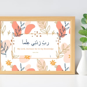 May include: A framed print with a white background and a floral pattern in shades of pink, peach, and gold. The print features an Arabic phrase that translates to "My Lord, increase me in my knowledge." The phrase is written in black and gold calligraphy. The print is framed in a light wood frame.