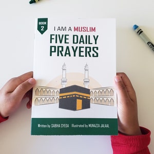 May include: A green and white book titled "I Am A Muslim: Five Daily Prayers" with an illustration of the Kaaba and minarets. The book is held by a child's hands. The text "Book 2" is in a green box on the cover.