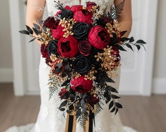 Puede incluir: Un ramo de novia en cascada con peonías y rosas de color rojo intenso, contrastadas con rosas negras y acentos dorados. Cintas negras y doradas caen del ramo, creando un aspecto dramático y elegante.