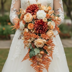 May include: A cascading bridal bouquet featuring a mix of orange, peach, and white flowers. The bouquet includes roses, dahlias, and fern accents. The bride is wearing a white lace wedding dress.