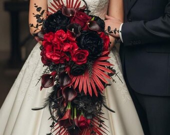 Puede incluir: Un ramo de novia en cascada con flores rojas y negras, incluyendo rosas y calas, con acentos de plumas negras y hojas de palma rojas. La novia lleva un vestido de novia blanco.