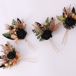 May include: Four hair pins featuring black rose details, gold-coloured leaves, and glittery gold and brown sprigs. The floral hair accessories are displayed on a white surface. Each pin has a gold-coloured double prong.