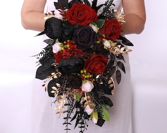 Puede incluir: Un ramo en cascada con rosas rojo oscuro, peonías negras y acentos de hojas doradas y rosa pálido. El arreglo incluye hojas y bayas oscuras, creando un diseño floral de inspiración gótica.