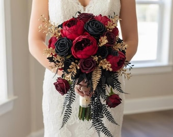 Puede incluir: Un ramo de novia con peonías y rosas rojas y negras, con detalles dorados. El ramo incluye hojas negras en forma de helecho. Un arreglo floral para una boda o una ocasión especial.