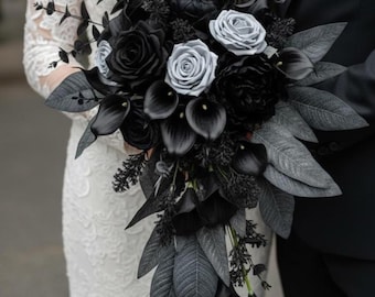May include: A bridal bouquet featuring black roses, calla lilies, and gray foliage. The arrangement includes a mix of textures and shades, creating a dramatic and elegant look. The bouquet is held by a person wearing a white lace dress.