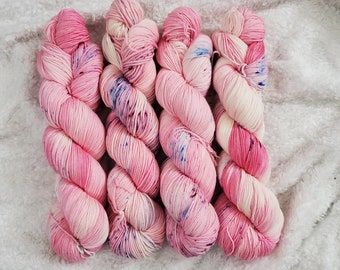May include: Four skeins of pink and white yarn with blue speckles. The yarn is arranged in a row, with the ends of the skeins overlapping.