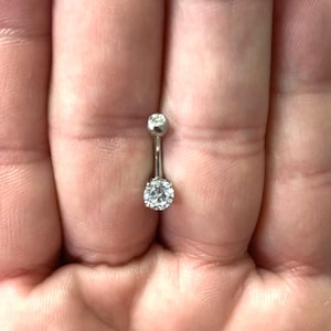 May include: A silver belly button ring with a clear round gem in the centre.