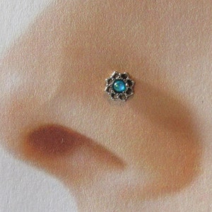 May include: A silver nose ring with a blue opal gemstone in the centre, surrounded by a decorative floral design.