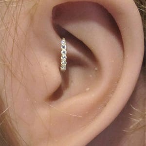 May include: A close-up of a person's ear with a small gold hoop earring with clear gemstones set in the hoop.