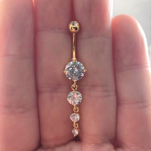 May include: Gold belly button ring with a dangling chain of clear round stones.