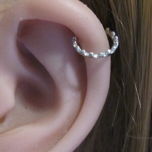 May include: A close-up of a person's ear with a small silver hoop earring. The hoop is made of a textured metal and has a slightly irregular shape.