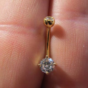 May include: Gold belly button ring with a clear round gemstone.