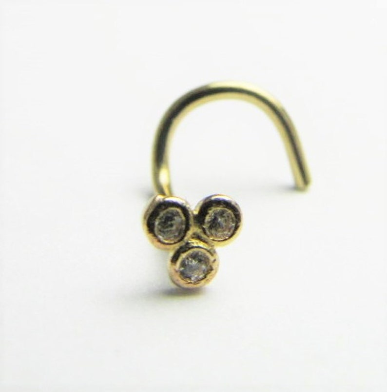 May include: Gold nose ring with three clear round stones.