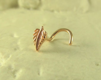 Könnte beinhalten: Ein goldener Nasenring mit einem Blattdesign. Der Ring besteht aus einem dünnen Draht und hat einen kleinen, zarten Blattanhänger am Ende.