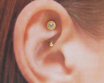 May include: Gold ear piercing with a small round clear stone in a decorative setting and a small gold ball on the other end.