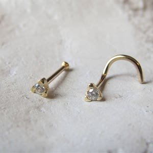 Può includere: Due anelli per il naso in oro con una piccola pietra preziosa trasparente al centro di ogni anello.