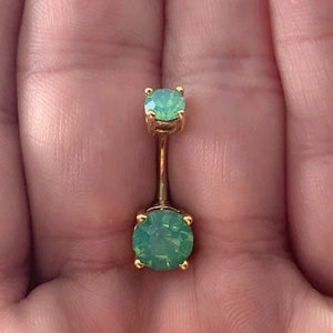 Peut inclure: Anneau de nombril en or avec deux pierres d'opale vertes.