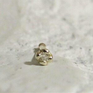 May include: A gold nose ring with a small diamond in the center. The ring is shaped like a flower.