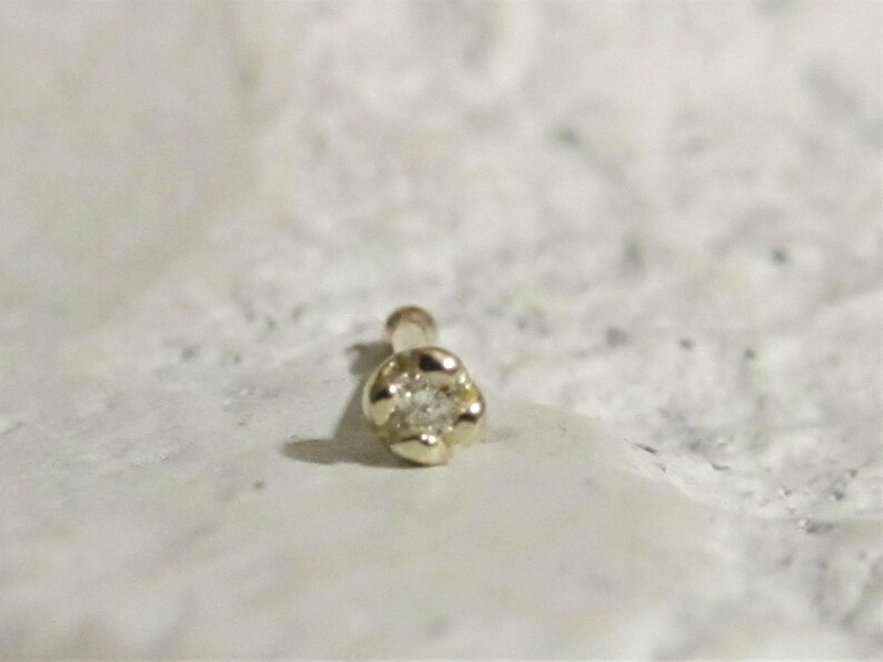 May include: A gold nose ring with a small diamond in the center. The ring is shaped like a flower.