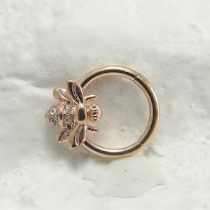 May include: Gold-toned hoop earring with a bee charm featuring clear rhinestones.