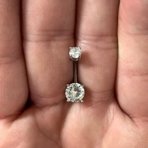 May include: A silver belly button ring with two clear round gemstones.